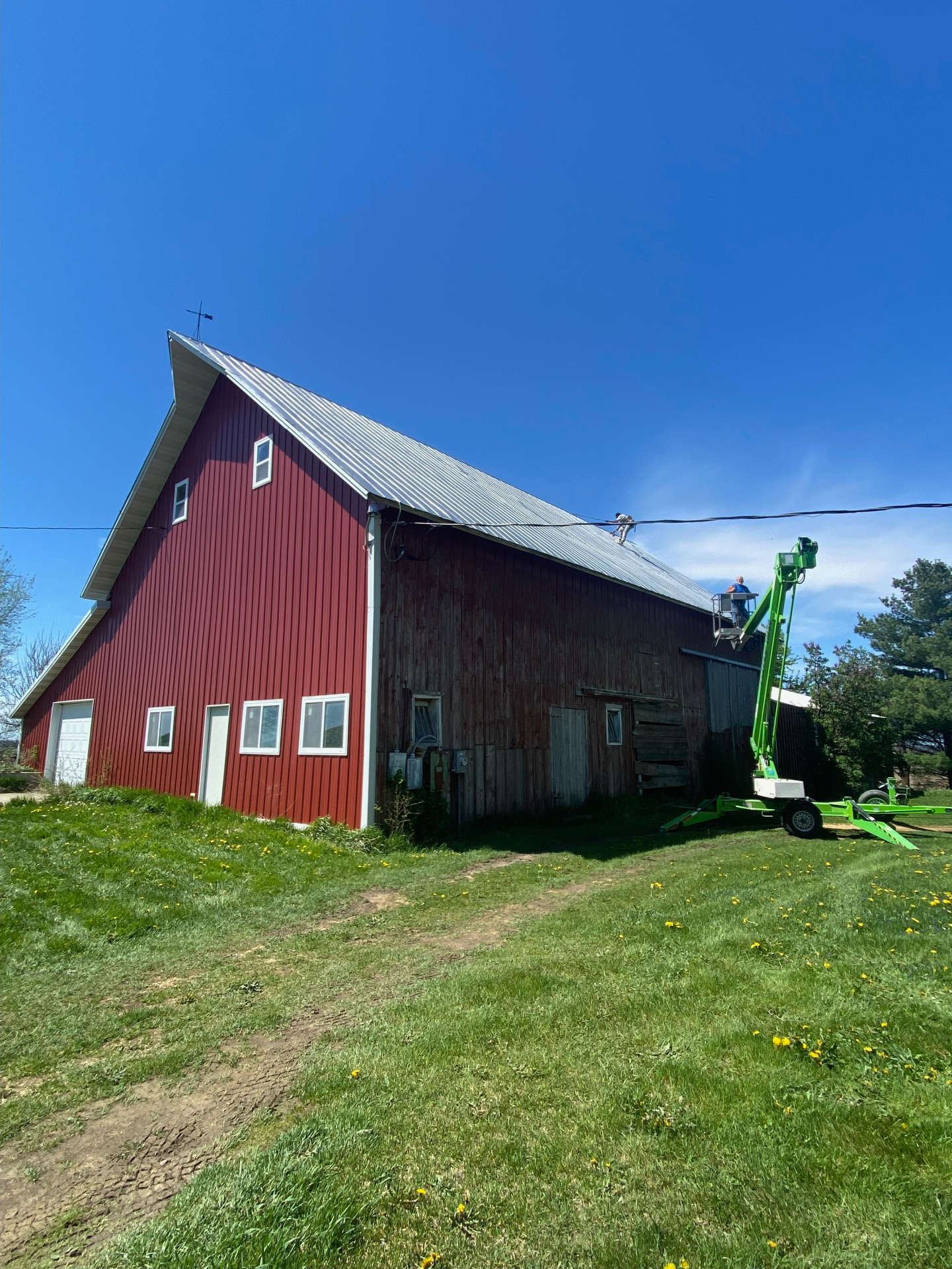 New metal roof on a red barn installed with a towable boom lift